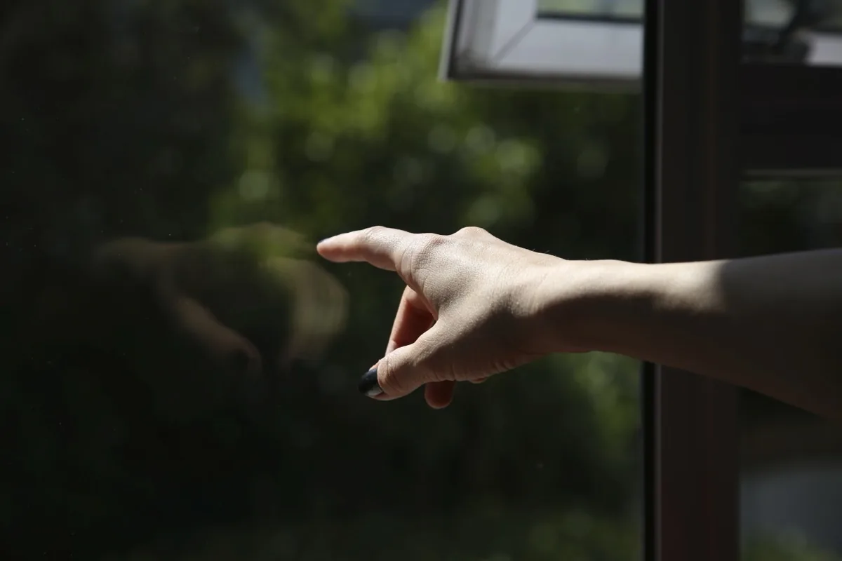 Hand against a window, pointing outside